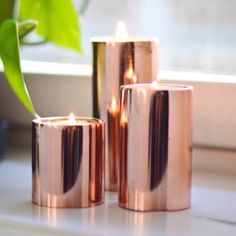 three copper colored candles sitting on top of a window sill next to a potted plant