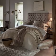 a bedroom with a large bed covered in beige blankets and pillows, next to a window