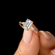 a woman's hand holding a ring with an emerald and diamond center stone on it