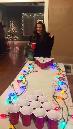 a woman standing in front of a table with cups on it and christmas lights strung across the table