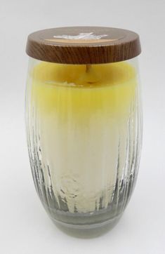 a glass jar with a wooden lid filled with yellow liquid and white frosted wax