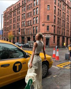 a woman walking down the street in front of a yellow taxi and some tall buildings