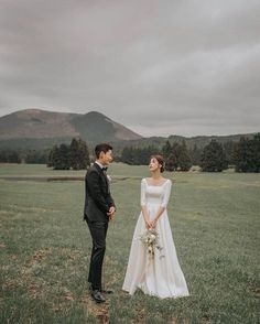 a bride and groom standing in the middle of a field with mountains in the background