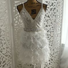 a white dress on display in front of a wall with lace and feathers around it