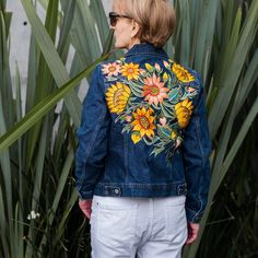 a woman wearing a jean jacket with sunflowers painted on the front and back