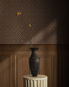 a black vase sitting on top of a table next to a wallpapered wall