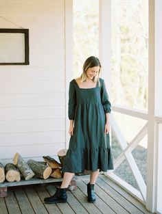 a woman in a green dress standing on a porch next to some logs and trees