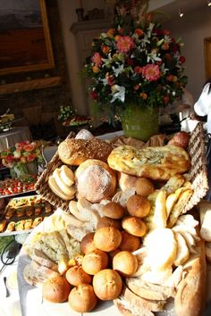 an assortment of breads and pastries on a table with flowers in the background