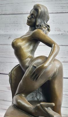 a bronze statue of a naked woman sitting on a chair with her hands behind her back