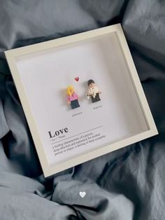 two small legos are in a shadow box on a bed with the word love written below them