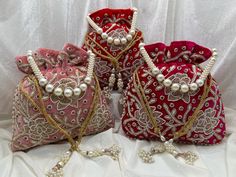 three purses with pearls on them sitting on a white cloth covered surface, one in red and the other in gold