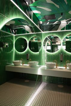 a green tiled bathroom with two sinks, mirrors and lights on the wall above them