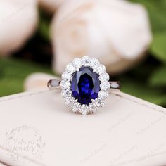 an oval shaped blue and white diamond ring on top of a box with flowers in the background