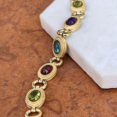 Estate/ vintage 14KT yellow gold Byzantine design, textured + cabochon, multi-gemstone link bracelet. Textured, shiny, and matte finishes on this piece. Slightly concave pieces with cabochon, amethyst, blue topaz, garnet, peridot, and citrine oval gemstones. Each gemstone measures: 7mm x 5mm; (8) total Rectangle byzantine + shiny open design links bracelet Measures 7.5", but fits shorter when clasped at the shorter length Weight: 22 grams Measures: 10mm wide Secure snap clasp Stamped 14K Great v Gold Oval Bracelet With Bezel Setting, Oval Gold Bracelet With Bezel Setting, Gold Elegant Cabochons With Bezel Setting, Elegant Gold Cabochons With Bezel Setting, Oval Gold Gemstones With Accents, Gold Jewelry With Gemstone Accents In Oval Cabochon, Elegant Multi-stone Oval Cabochon Jewelry, Gold Jewelry With Gemstone Accents And Oval Cabochon, Gold Jewelry With Gemstone Accents