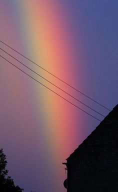 a rainbow appears in the sky over a house and power lines at sunset or dawn