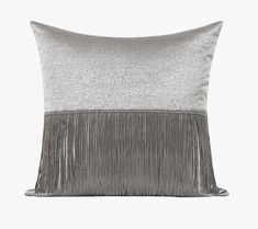 a silver and black pillow with fringes on the front, sitting against a white background