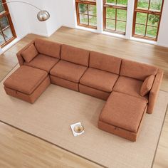 a brown sectional couch sitting on top of a hard wood floor next to a window