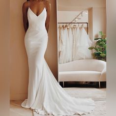 a woman standing in front of a mirror wearing a white wedding dress with spaghetti straps