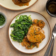 two plates with meat, vegetables and gravy on them next to silverware