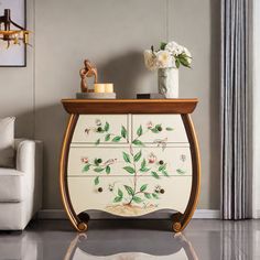 a white cabinet with flowers painted on the front and drawers, sitting in a living room