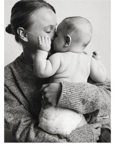 a woman holding a baby in her arms and kissing it's face with both hands