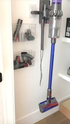 a blue and silver vacuum is on the floor in front of a white wall with shelves