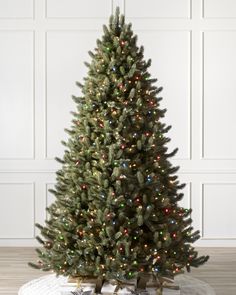 a small christmas tree with multi - colored lights is on the floor in front of a white wall