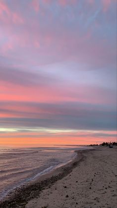 the sky is pink and purple as the sun sets on the beach in front of the ocean