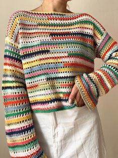 a woman wearing a multicolored crochet sweater and white skirt with her hand on her hip