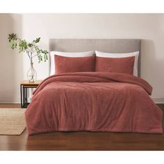 a bed with a red comforter and pillows in a room next to a plant