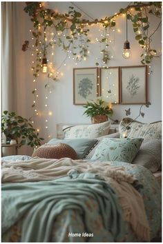 a bed covered in lots of pillows and blankets next to a wall with lights hanging from it