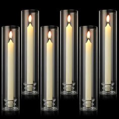 four candles are lined up next to each other in clear glass holders on a black background