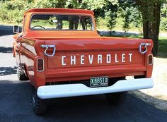 an old red chevrolet pickup truck parked on the side of the road with trees in the background