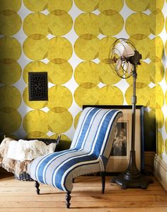 a striped chair in front of a wall with yellow circles on it and a fan