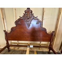 a wooden headboard with ornate carvings on the top and sides, in an unfinished room