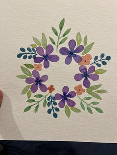 a hand holding up a piece of paper with watercolor flowers on it