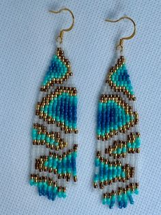 two pairs of beaded earrings on a white surface with blue and gold beads hanging from them