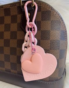 a pink heart shaped keychain hanging from a brown purse