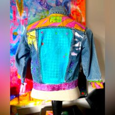 the back of a jean jacket on display in front of a colorful painting and other items