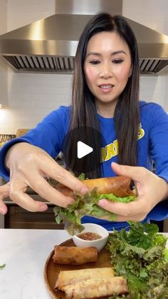 a woman in a blue shirt is holding a sandwich and some lettuce on a plate