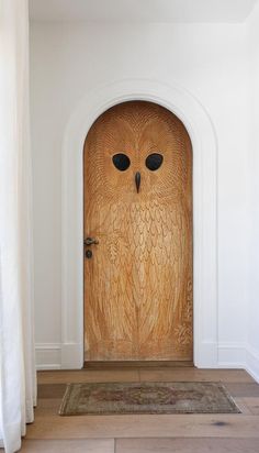 an owl carved into the side of a wooden door in a white walled entryway