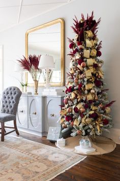 a decorated christmas tree in the corner of a living room with a chair and mirror