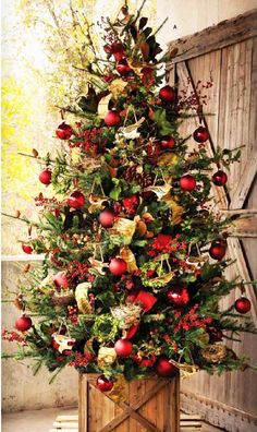 a christmas tree with red ornaments and greenery in a wooden box on the floor