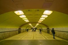 people are walking through a tunnel with yellow walls and lights on either side of the walkway