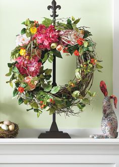 a wreath with flowers on top of a mantle next to an egg in a basket