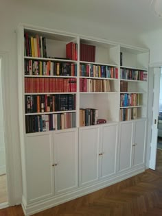 a white bookcase filled with lots of books on top of wooden floored floors