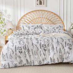 a bed with white and black floral print on it, next to a wicker headboard