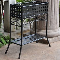 a black metal bench sitting next to a tall stone pillar and planter on the sidewalk