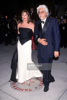 an older man and woman standing next to each other on the red carpet in front of photographers