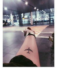 a person's arm with a small airplane tattoo on the left side of their wrist